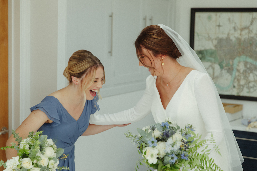 a bride and her bridesmaid laugh together before the ceremony