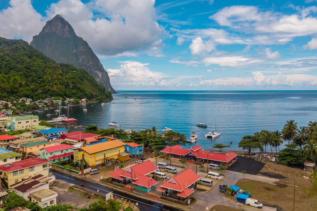 St Lucia's iconic mountains stand in the background, and a town of colourful houses can be seen in the foreground on the coast