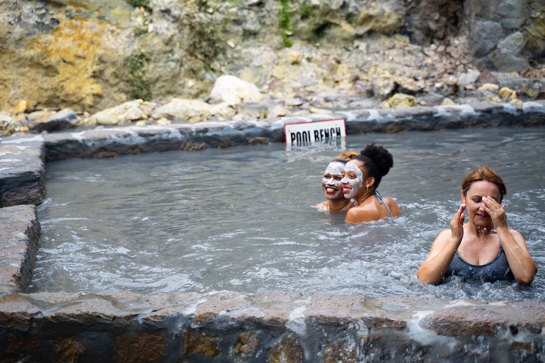 One of the great things to do in St Lucia is bathe in the sulphur springs. The image shows two people enjoying the springs smiling at the camera.